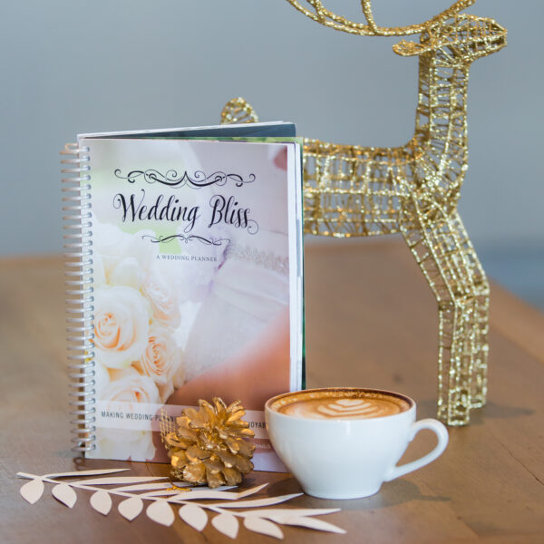 Wedding planner on wooden table with gold deer, paper flowers and a cup of coffee