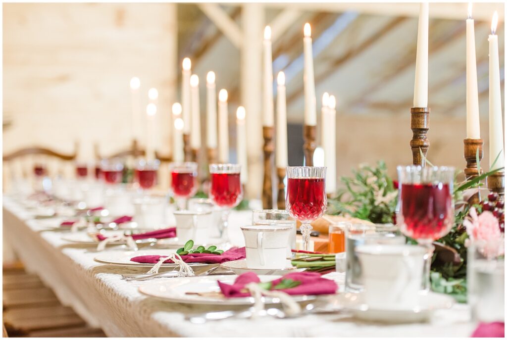 Beautiful wedding reception table setting with burgundy napkins, goblets, and long white taper candles with wooden bases