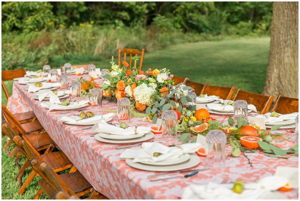 Beautiful coral colored outdoor wedding reception table setting with fresh flowers, greens and fruit