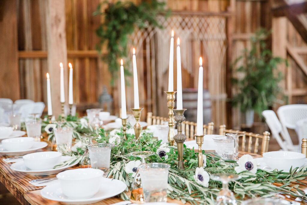 Gorgeous wedding reception tablescape with white anemone flowers, greenery, long white taper candles and brass candlesticks